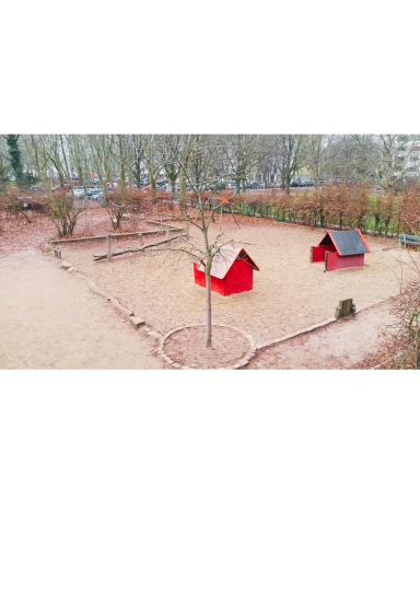 Spielplatz mit zwei roten Hütten und Sandfläche, umgeben von Bäumen.